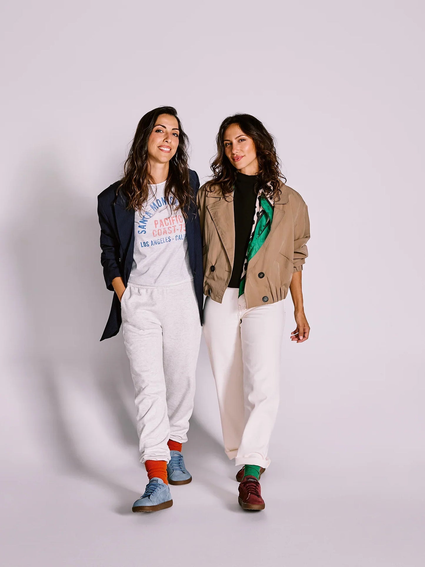 Duas mulheres sorridentes a caminhar, uma a usar sapatilhas MUM Barefoot Diana Wine bordô e outra sapatilhas azuis.