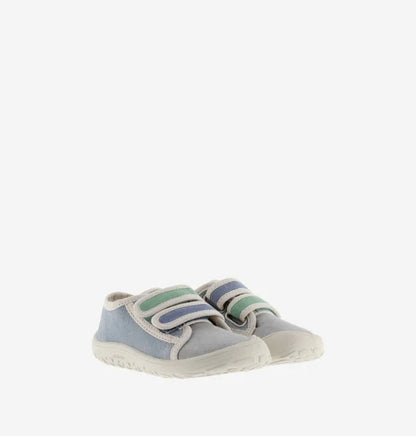 Par de sapatilhas infantis de lona, azul e cinzenta, com detalhes em verde e azul nas tiras de velcro, colocadas lado a lado em fundo branco.