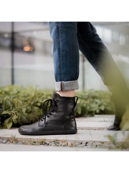 Pé a caminhar em passadiço exterior com vegetação, mostrando a bota preta de atacadores Angles Orpheus zip winter em uso.