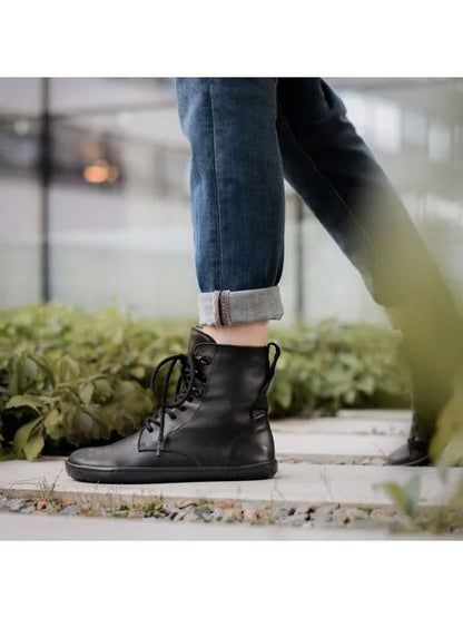 Pé a caminhar em passadiço exterior com vegetação, mostrando a bota preta de atacadores Angles Orpheus zip winter em uso.
