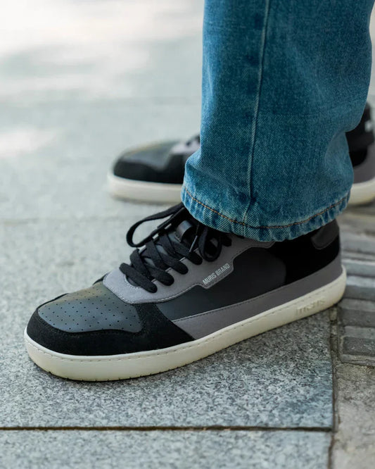 Detalhe da sapatilha Muris Majorca Black em uso, calçada com calças de ganga, mostrando o design barefoot e o fecho de velcro.