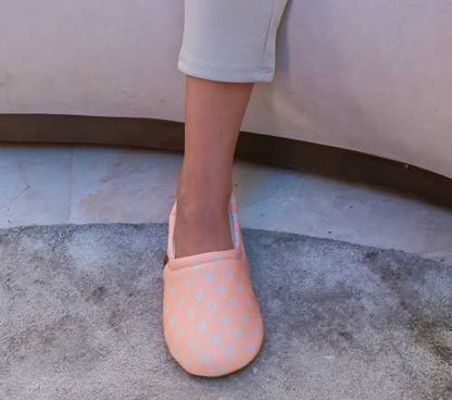 Pé de criança a usar a pantufa Slip Stop Booties cor de rosa claro com corações, em cima de um tapete cinzento, demonstrando o uso interior.